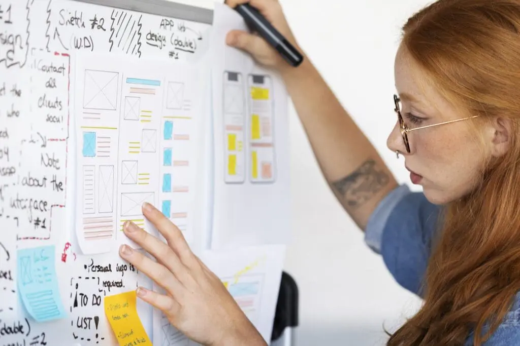 Woman writing on a whiteboard illustrating concepts related to UI/UX design