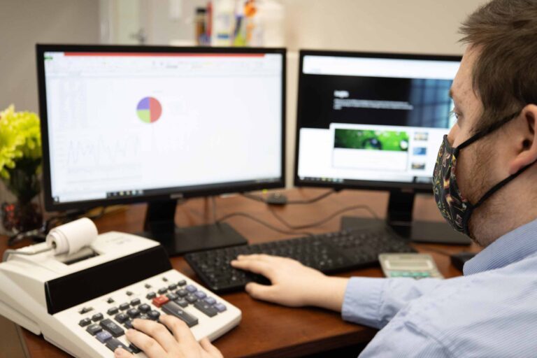 an account assistant working his computer and a receipt printer while wearing a mask