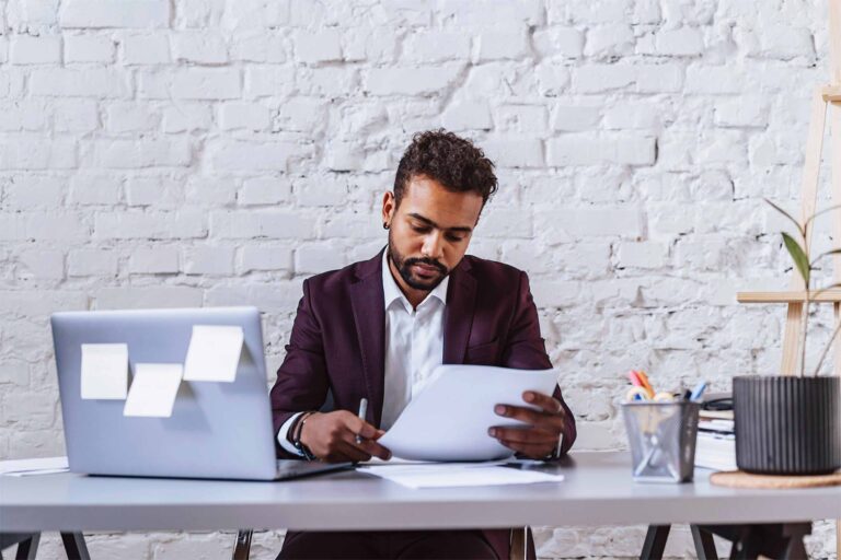 a man in suit checking some papers with a laptop in front of him