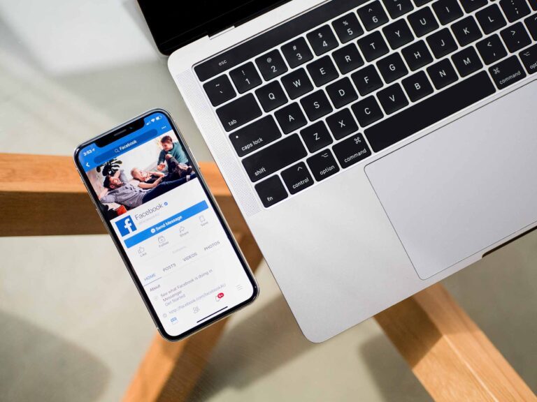a phone with Facebook page open and a laptop beside it