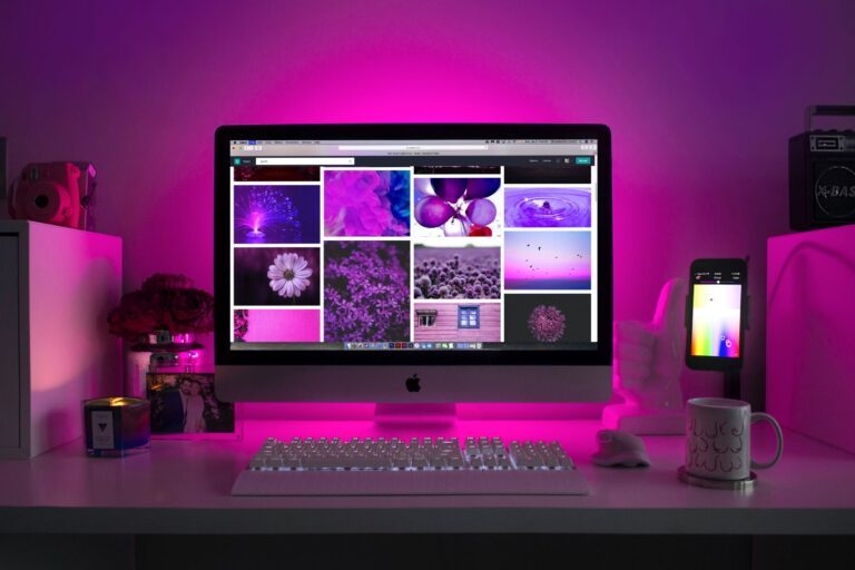 an image of a computer setup surrounded by different items with a purple or pink light emitting from the back of monitor