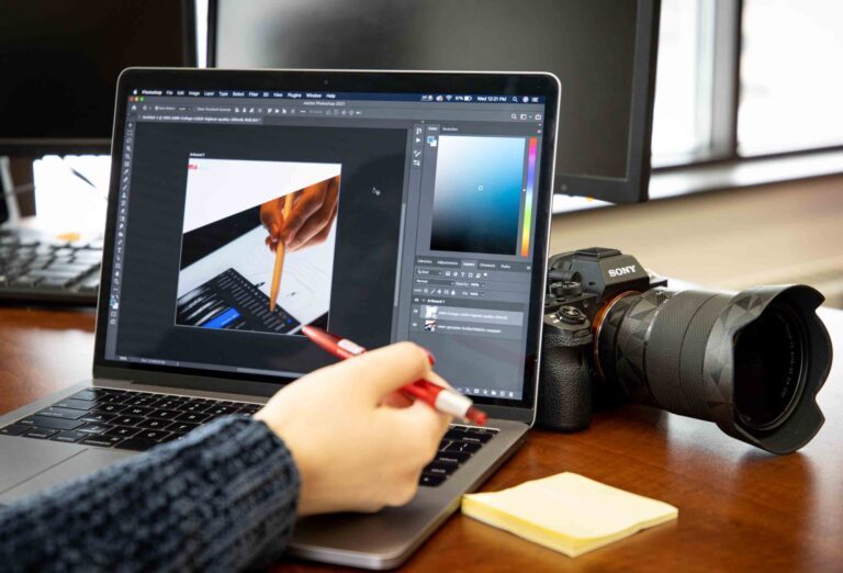 a person using a laptop with a notepad beside it and a camera behind the laptop