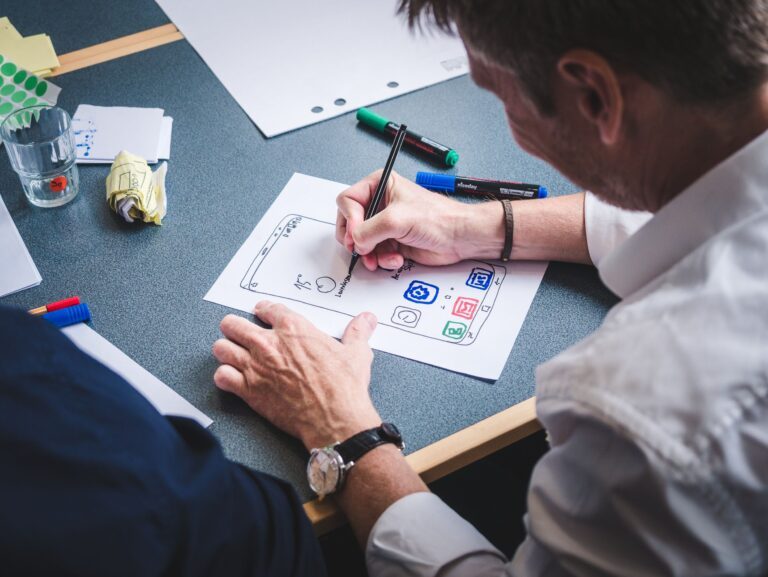 a man drawing the layout of a phone with all the apps on a piece of paper