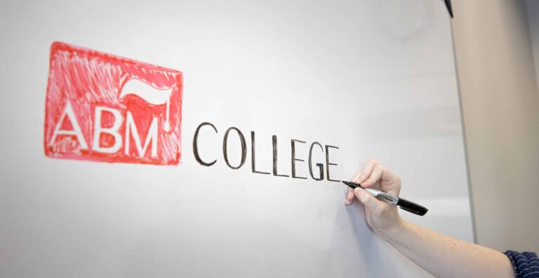 a person writing and drawing the ABM College logo on a whiteboard