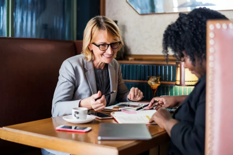 two women in suit discussing with each other and writing down notes